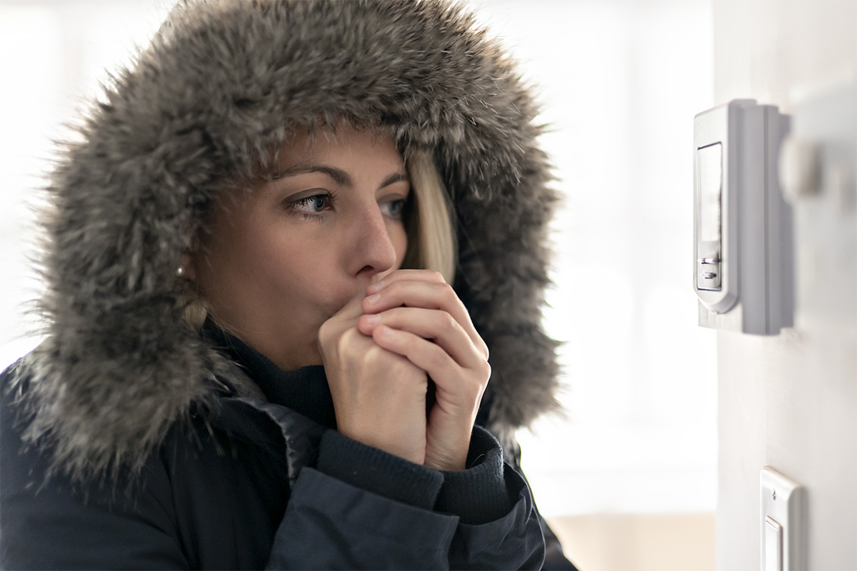 Woman feeling cold wearing a coat in front of a thermostat